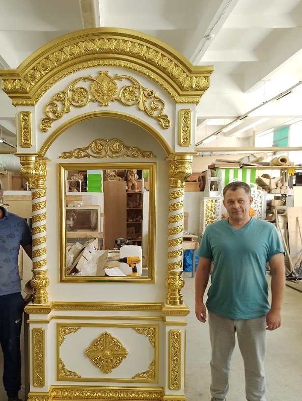 мастер в цеху семейной мастерской рядом с белым храмовым киотом с резьбой и элементами золочения