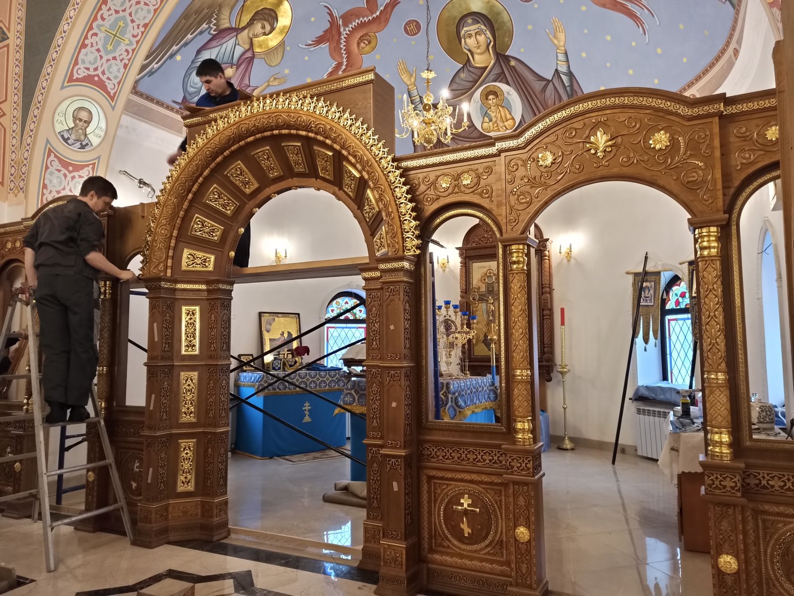двое мастеров собирают центральную часть иконостаса из дуба с резьбой и золочением в помещении храма